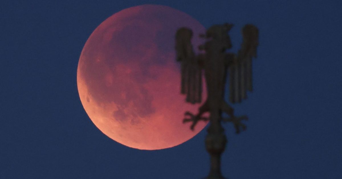 The moon glows red behind the metal sculpture of an eagle over Oberbaumbrücke bridge during a lunar eclipse on September 07, 2025, in Berlin, Germany (Cover Image Source: Getty | Sean Gallup)