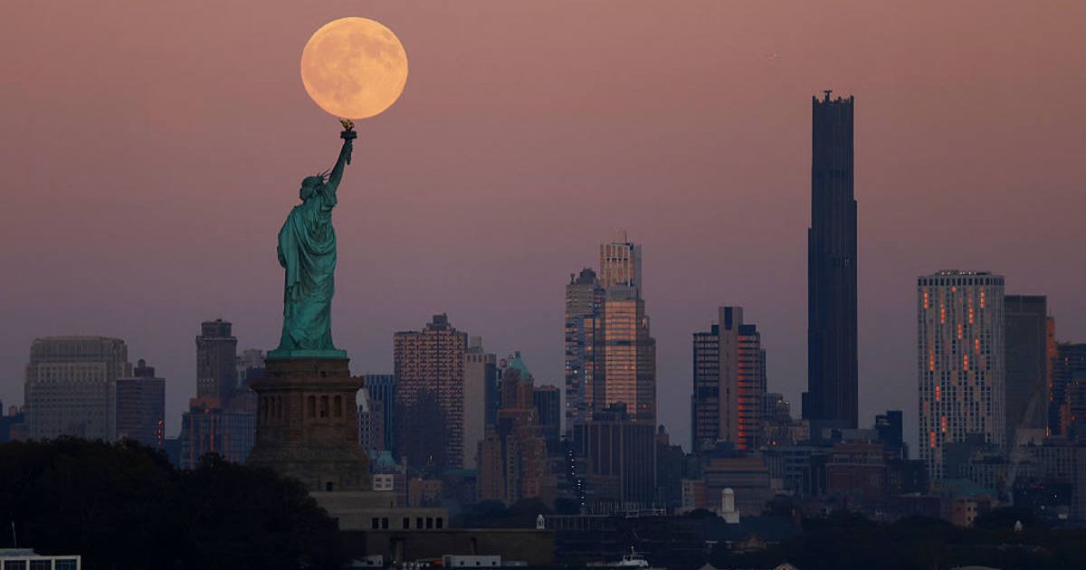 The Harvest Supermoon rises behind the Statue of Liberty and the Brooklyn skyline in New York City (Image Source: Getty | Gary Hershorn)