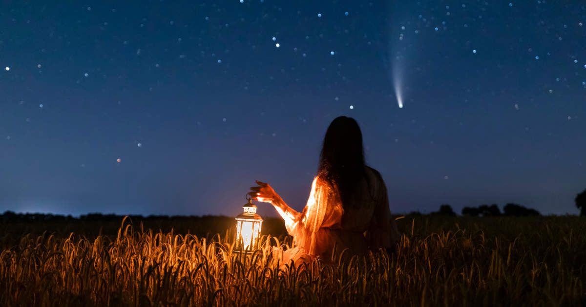 Woman in field with lantern on background of a Comet (Representative Cover Image Source: Getty | Anton Petrus)