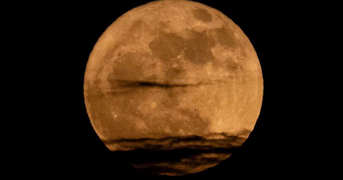 The Strawberry Moon, appearing unusually low in the sky and partially veiled by a horizontal band of clouds, is seen fully risen on June 11, 2025, in Chongqing, China. (Photo by Cheng Xin / Getty Images)