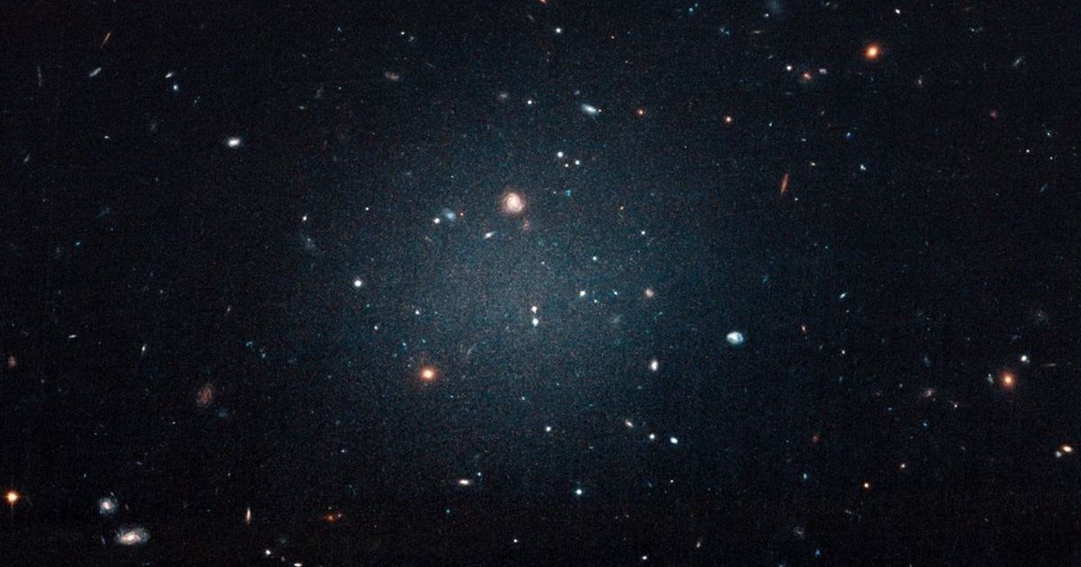 Image of the NGC 1052-DF2 Ultra Diffuse Galaxy that started the chain of discoveries of galaxies lacking dark matter. (Cover Image Source: NASA, ESA, and P. van Dokkum (Yale))