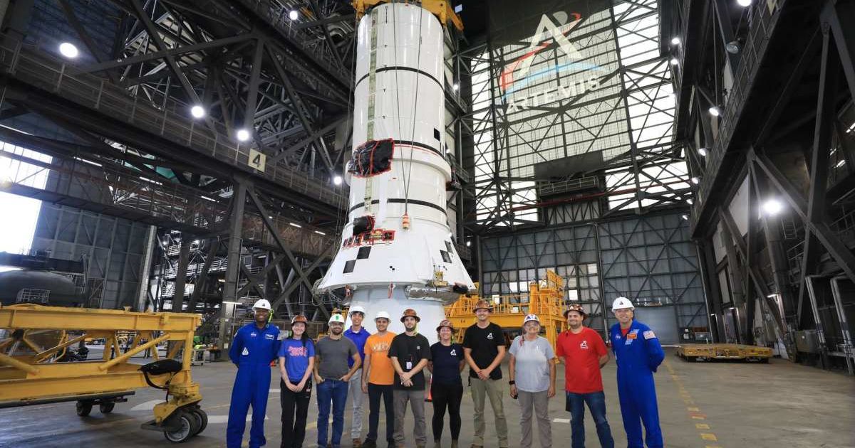 Artemis III's Randy Bresnick (far right) and Andre Douglas (far left), pose with Exploration Ground Systems team in front of the right-hand aft assembly of SRB for Artemis III SLS rocket at the VAB. (Image Source: NASA | Kim Shiflett)