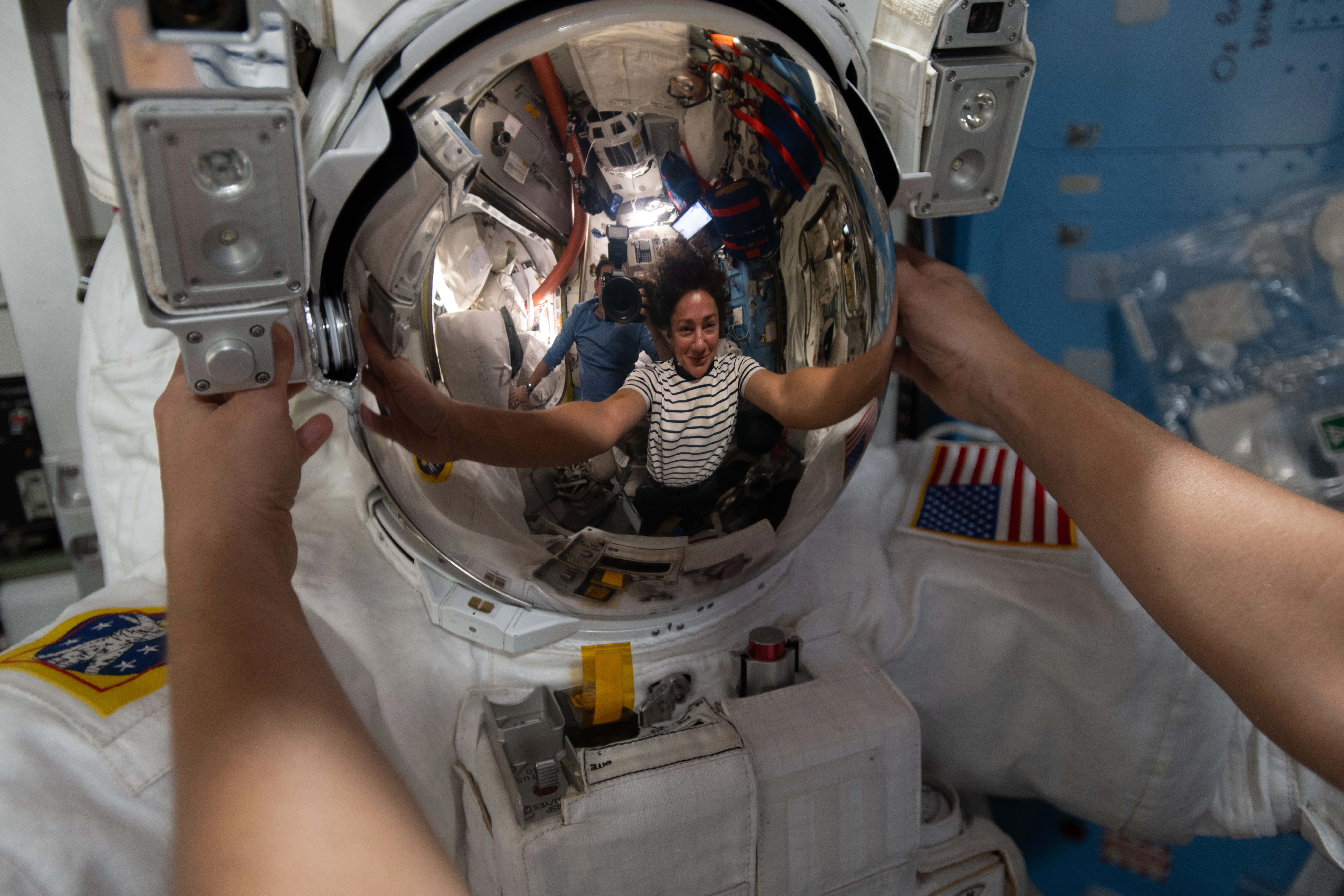 NASA astronaut Jessica Meir's reflection is visible in a helmet as she works on her spacesuit inside the International Space Station’s Quest airlock, March 2026.