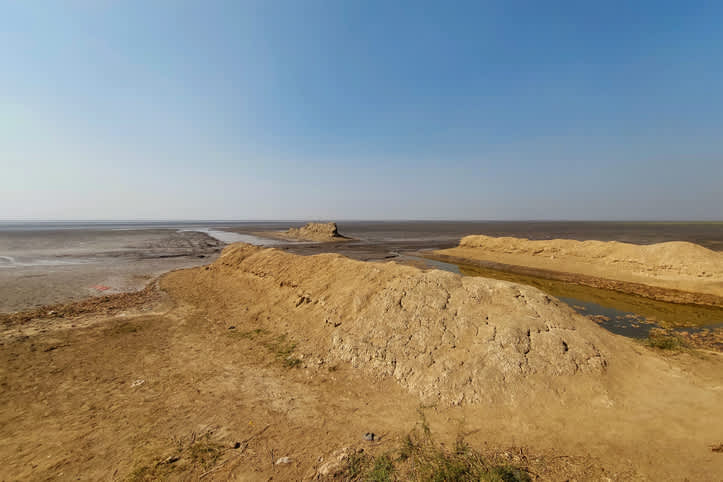 Scenic view of a dry, cracked beach with small water channels under a clear blue sky