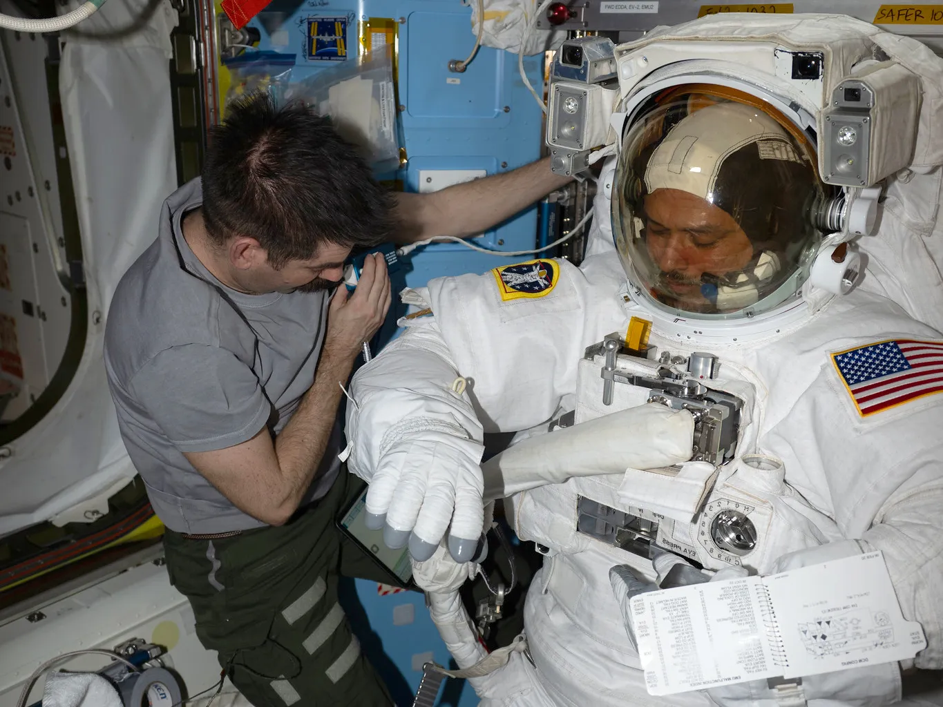 Jack Hathaway assists Anil Menon inside the Quest airlock as he tried on a spacesuit to verify its comfort, mobility, and functionality to prepare for a spacewalk.
