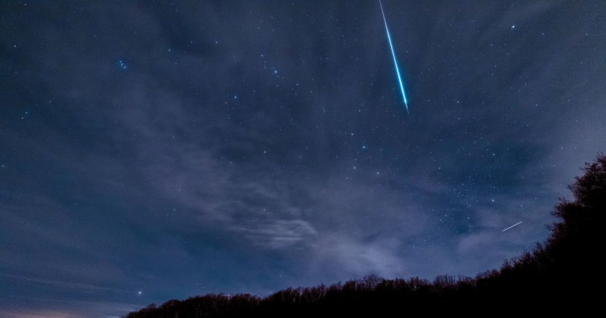 Breathtaking view of a meteor streaking across a starry and cloudy night sky above dark silhouettes of trees. (Representative Cover Image Source: Roy S./Pexels)