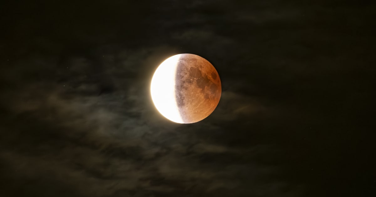 A close-up of a lunar eclipse on a cloudy night. During a deep partial eclipse, a tiny portion of the Moon is illuminated while the rest of the lunar surface appears coppery red. — (Cover Image Source: Nicola Colombo/Getty Images)