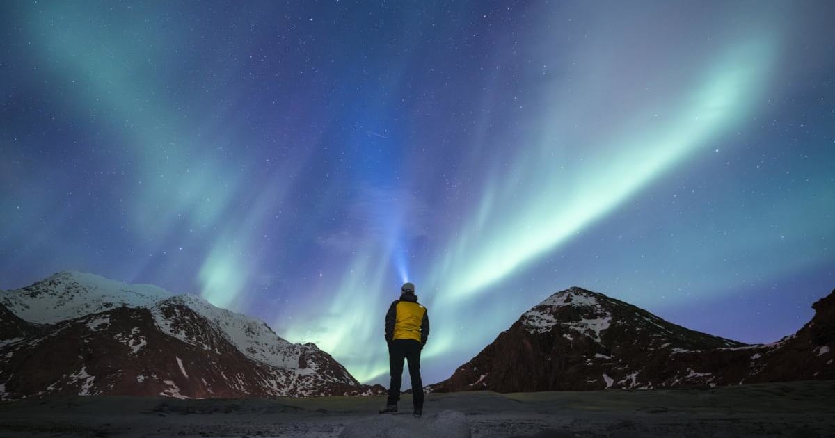 A person admiring the Northern Lights (aurora borealis) in Lofoten, Norway. (Cover Image Source: Getty/Marco Bottigelli)