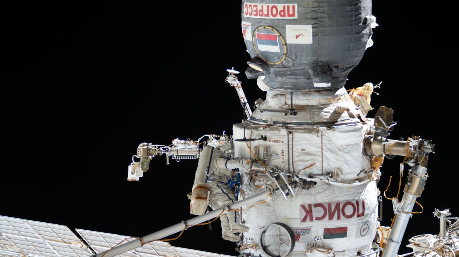 International Space Station's Poisk module seen with a Soyuz spacecraft docked to it, along with a Roscosmos cosmonaut performing a spacewalk. (Image Source: NASA)