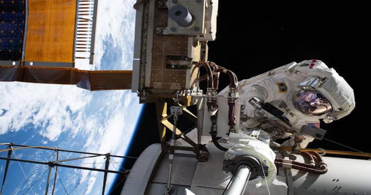 An astronaut conducts a spacewalk outside the International Space Station, with Earth visible in the background.  (Image Source: NASA)